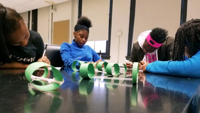 Four girls seated around a classroom table covered in construction paper models.