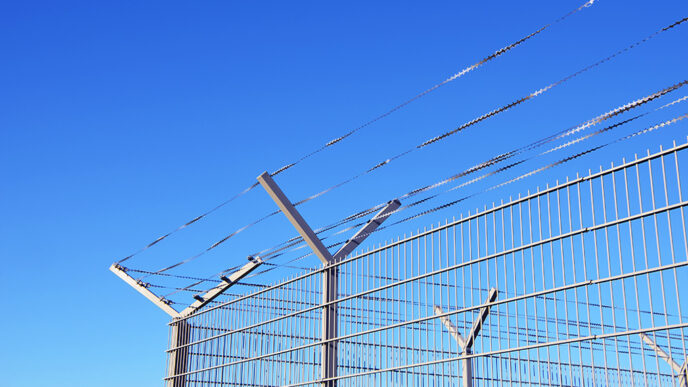 A prison yard fence against a blue sky.