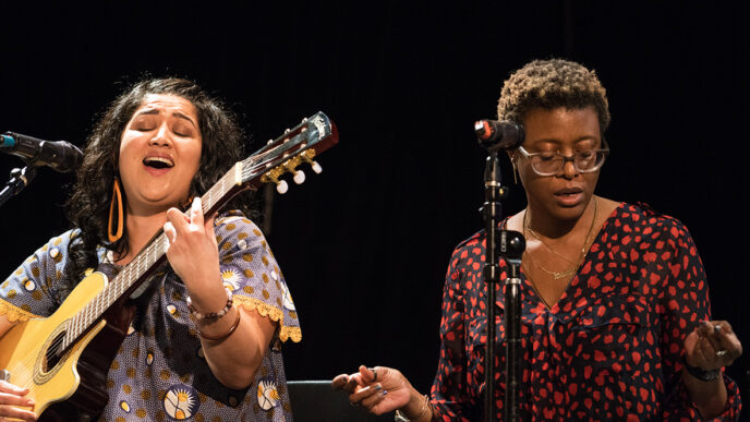 Two women sit on stage in front of microphones.