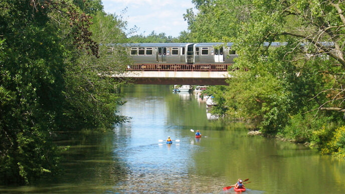 An elevated train crosses the Chicago River while kayakers paddle beneath the rail bridge