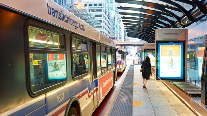 Two CTA buses stationed outside a bus stop in downtown Chicago. A passenger walks by on the right.