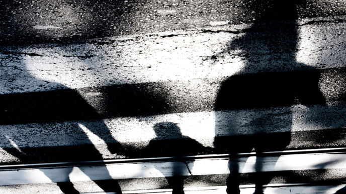 Shadows of two adults and a child holding hands over a crosswalk