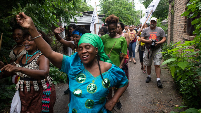 A procession of people march through a residential alley.