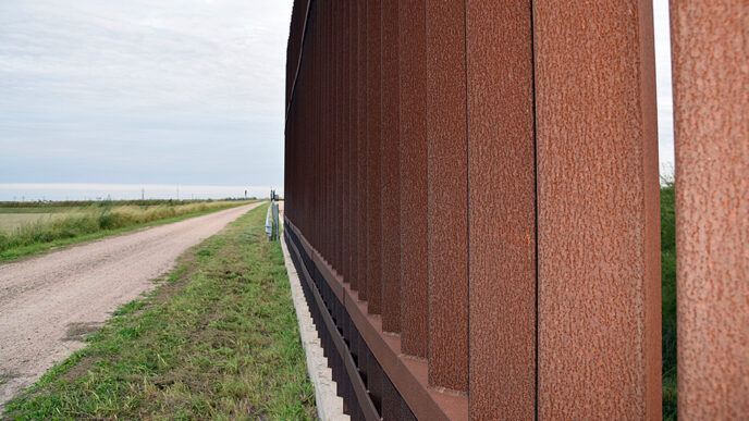 A road runs beside the metal posts of the border fence between Donna.