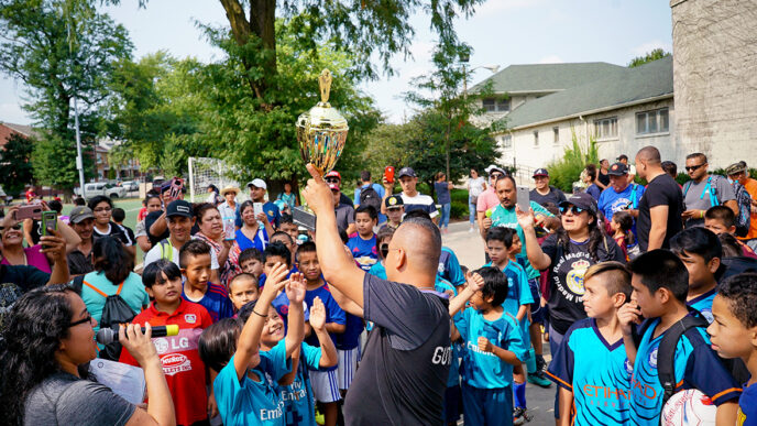 A man in a soccer jersey holds a trophy overhead.