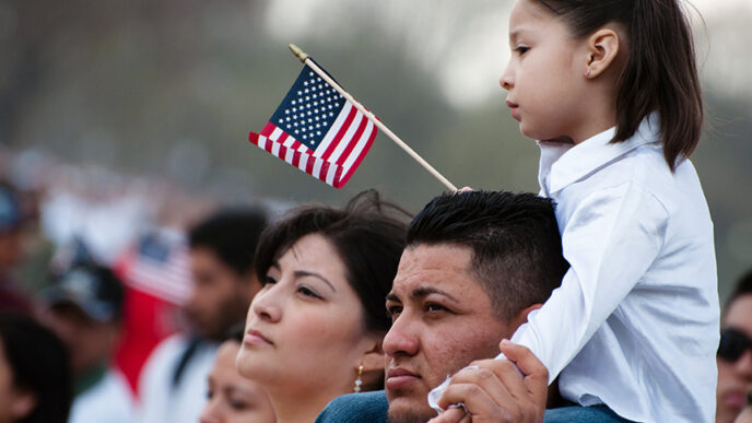 A couple stand side-by-side with their young daughter on the man's shoulders.