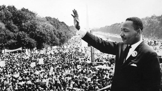 Rev. Dr. Martin Luther King Jr. stands on a podium overlooking the crowd at the 1963 March on Washington|Four men.