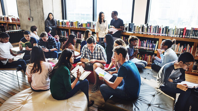 Young adults read and talk in small groups seated in a college library.