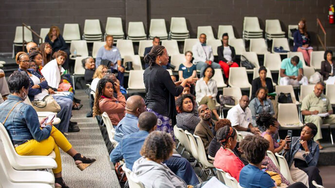 A speaker holding a microphone stands in the middle of a seated crowd in a lecture|A man stands at a podium.