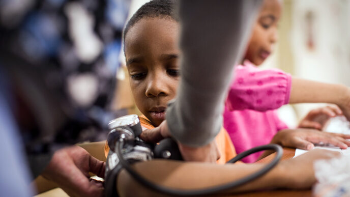 A young boy watches the hands of a nurse fastening a blood pressure cuff around his arm.