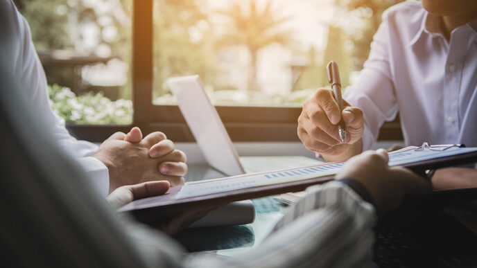 Close-up of a financial document with one person pointing out information to two other people.