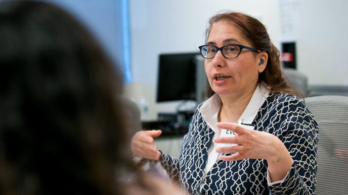 A seated woman gestures with her hands while talking to another person.