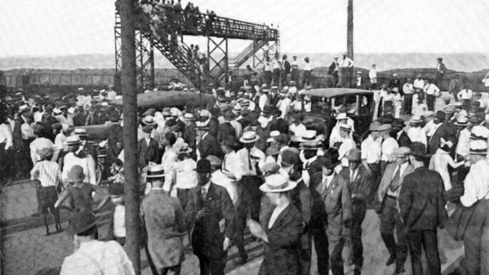 Black-and-white archival photo showing a large crowd of men standing at a road crossing.