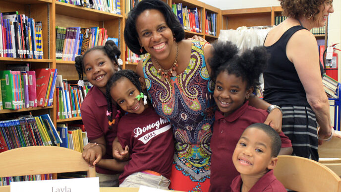 A woman and a group of kids smile together at a table in a school library|Head shot of Liz Thompson.