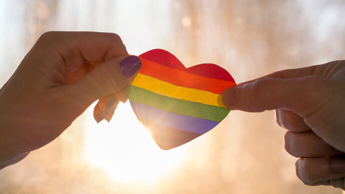 Two hands hold up a rainbow-striped heart.