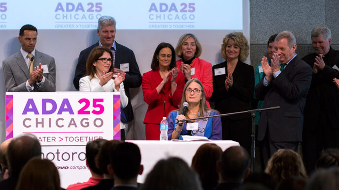 A group of people gathered behind a podium with a sign reading ADA 25 Chicago as one women speaks into a microphone|A group of people gathered behind a podium with a sign reading ADA 25 Chicago as one women speaks into a microphone.