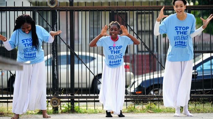 Three young dancers perform outside wearing t-shirts that say Stop The Violence.