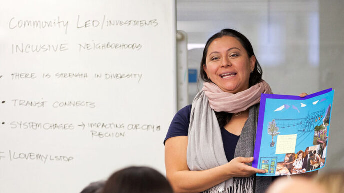 A woman stands in front of a whiteboard facing a room of seated people|A small outdoor market in a city lot.