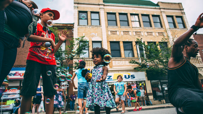 A little girl reaches for a bubble on a busy block celebrating a street fair