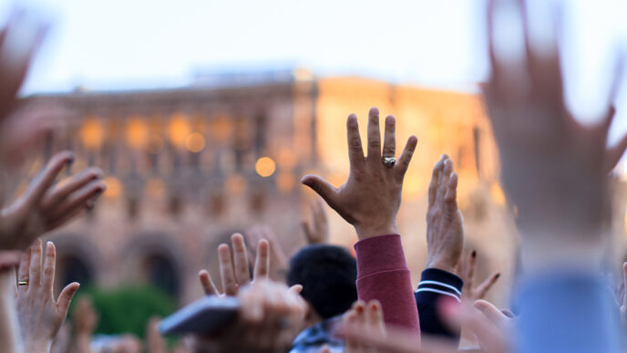 A crowd of people outdoors raising their hands.