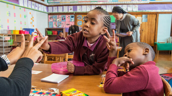 Two children and a teacher sit at a classroom table.