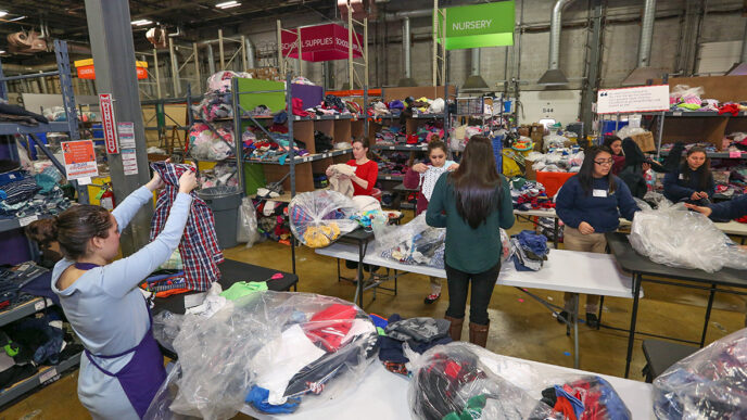 A group of women stand around tables in a warehouse.