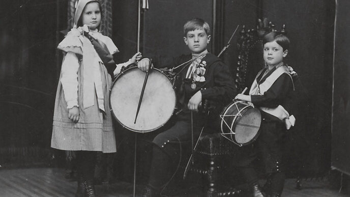 Old black-and-white photo of three children holding drums and American flags.